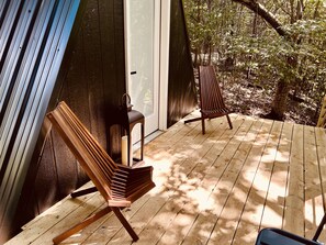A wooden deck with two Adirondack chairs and a lantern, surrounded by trees. - The EH Frame with Tree Pod in the woods! (Fountain Run)