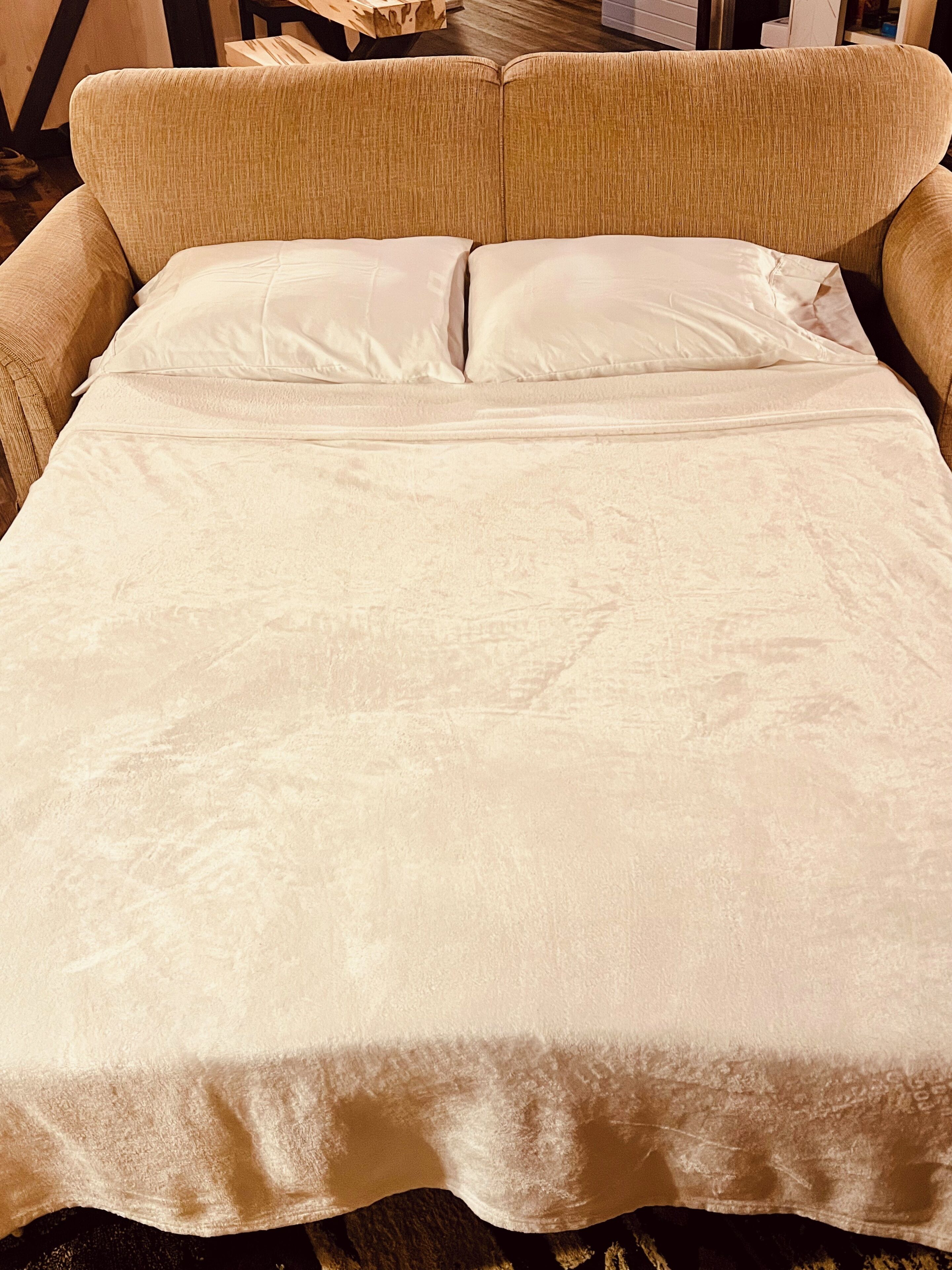 A bed with a beige bedspread and pillows, a wooden headboard, and a wooden floor.