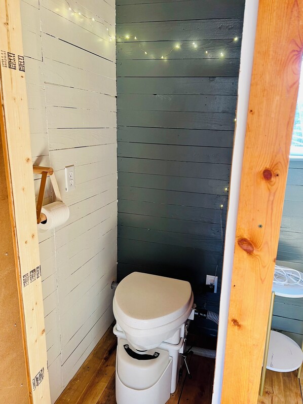 Ein kleines, kompaktes Badezimmer mit Toilette in Weiß, Holzboden und einer weißen Wand mit Holzpaneelen.