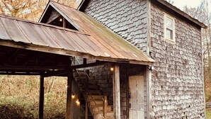 A rustic cabin with a wooden exterior, a metal roof, and a wooden staircase leading to a door. - Rustic Old Mill Tiny Home (Fountain Run)