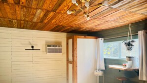 A room with wooden flooring, a ceiling fan, a window with a view, a small table, and a chair. - Rustic Old Mill Tiny Home (Fountain Run)
