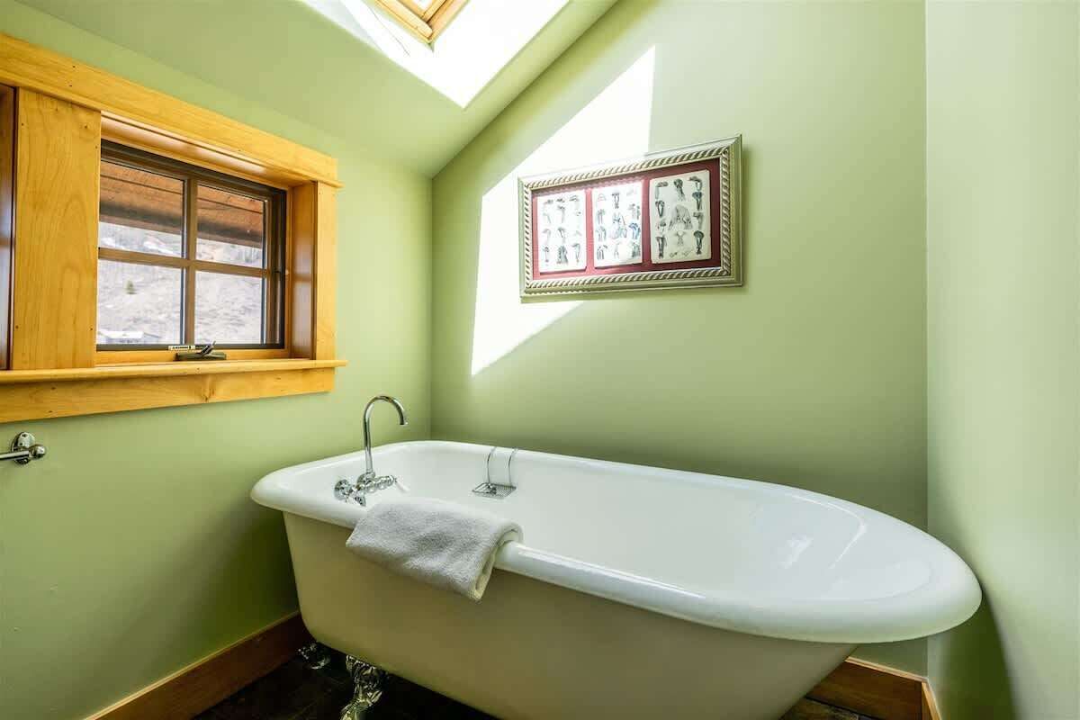 A bathroom with a freestanding bathtub, a window with a wooden frame, and a framed picture on the wall.