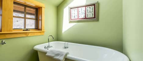 A bathroom with a freestanding bathtub, a window with a wooden frame, and a framed picture on the wall.