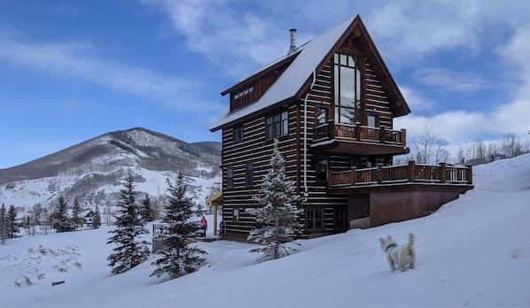A log cabin with a balcony, surrounded by snow-covered mountains.