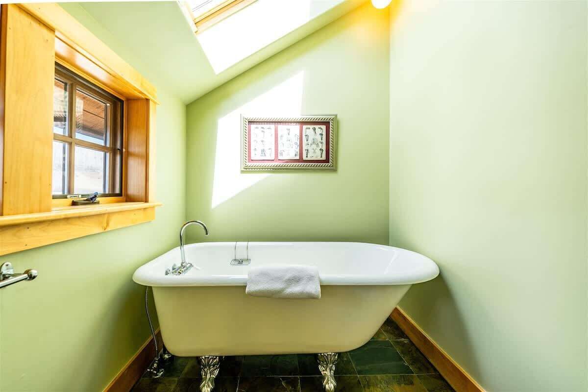 Une salle de bain avec une baignoire sur pieds, une fenêtre avec un cadre en bois et un tableau encadré au mur.