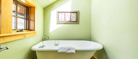 Une salle de bain avec une baignoire sur pieds, une fenêtre avec un cadre en bois et un tableau encadré au mur.