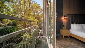 Un balcón con baranda de metal que da a un jardín y una cama con cabecera de madera.