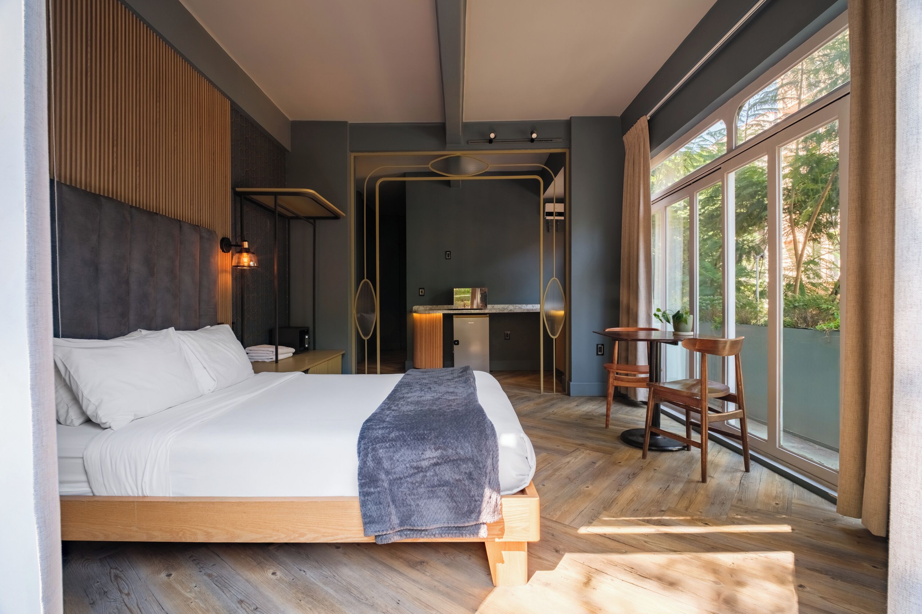 Une chambre moderne avec un grand lit, un bureau et une vue sur la verdure par la fenêtre.