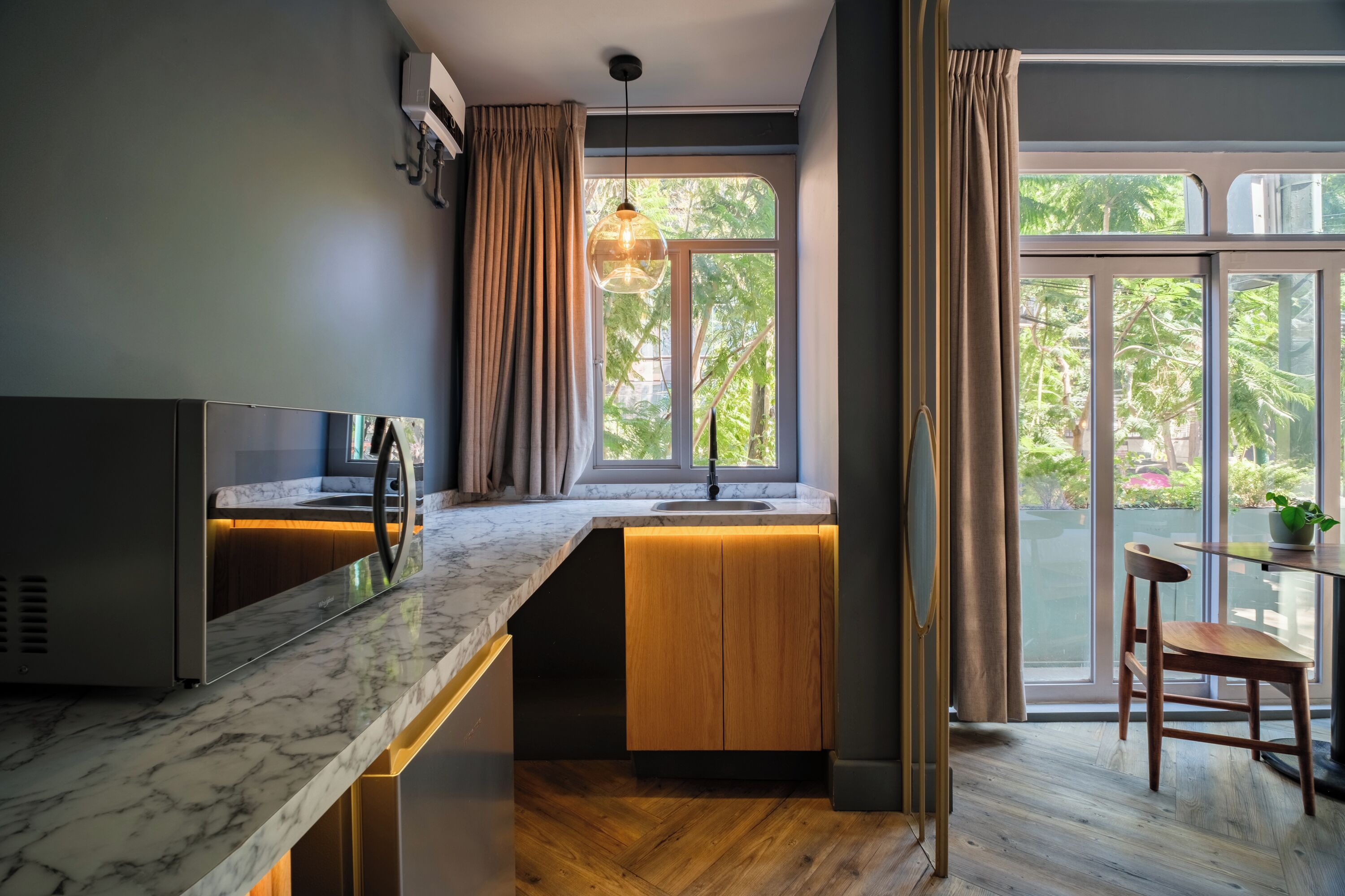 A modern kitchen with a marble countertop, wooden cabinets, and a window overlooking greenery.