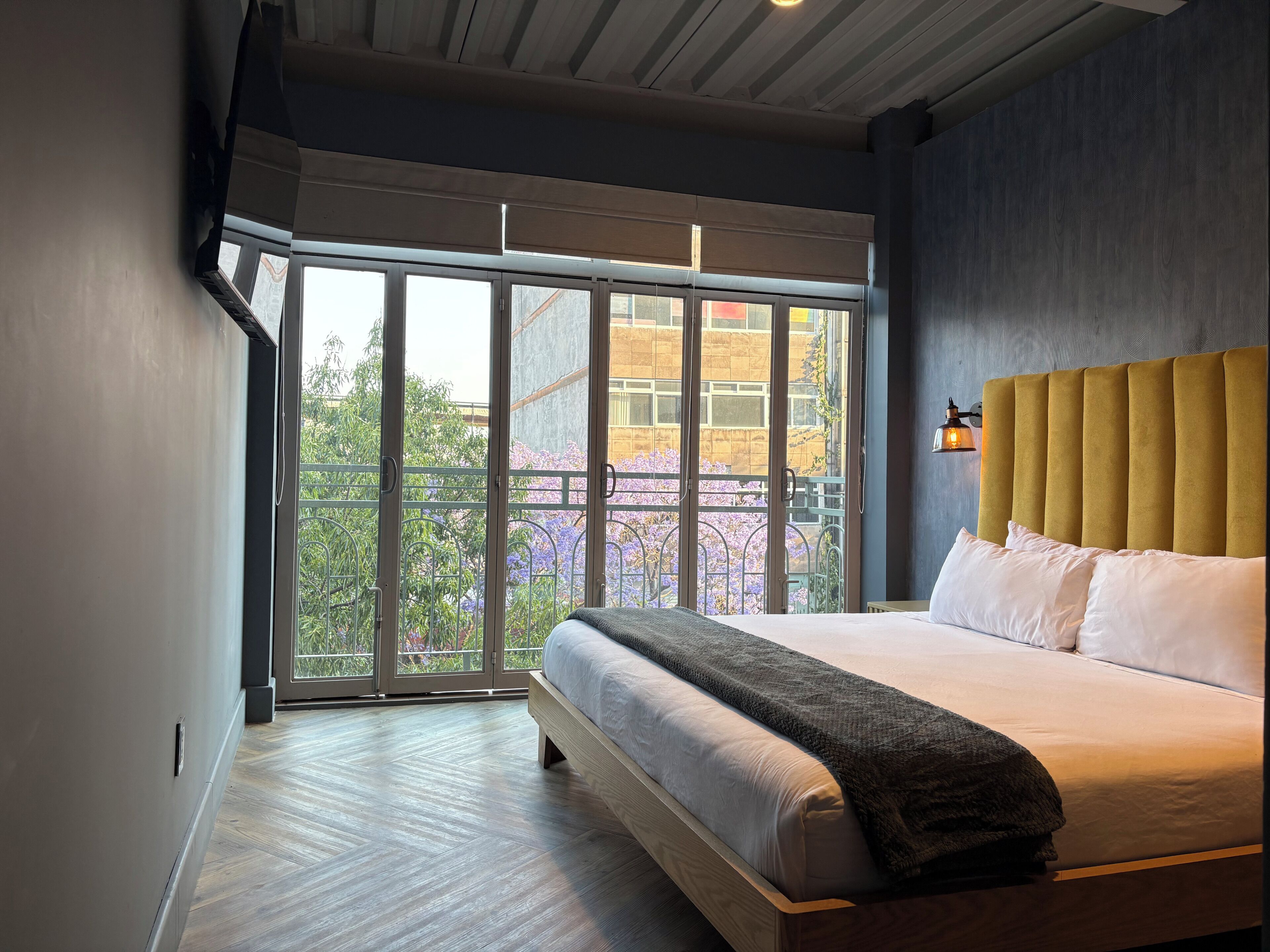 Een slaapkamer met een groot raam, een bed met witte beddengoed en een geel hoofdeinde.