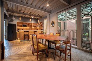 A spacious dining area with a wooden table and chairs, a kitchen in the background, and large windows with a view of the outside. - Pandora House (Mexico City)