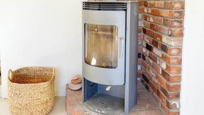 A wood-burning stove with a chimney, a brick wall, and a woven basket.