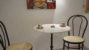 A small dining area with a round table and two chairs, a wall-mounted coffee-themed artwork, and a single light fixture. - Cozy vacation apartment on the farm - vacation for the whole family (Argenbühl)