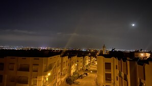 Vista notturna di una città con edifici illuminati e una luna crescente nel cielo.