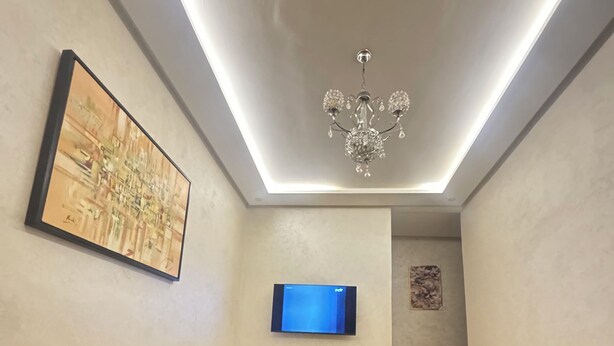 Un soggiorno moderno con due divani gialli, un tavolino in vetro con un vaso e un telecomando, una TV a schermo piatto e un lampadario.