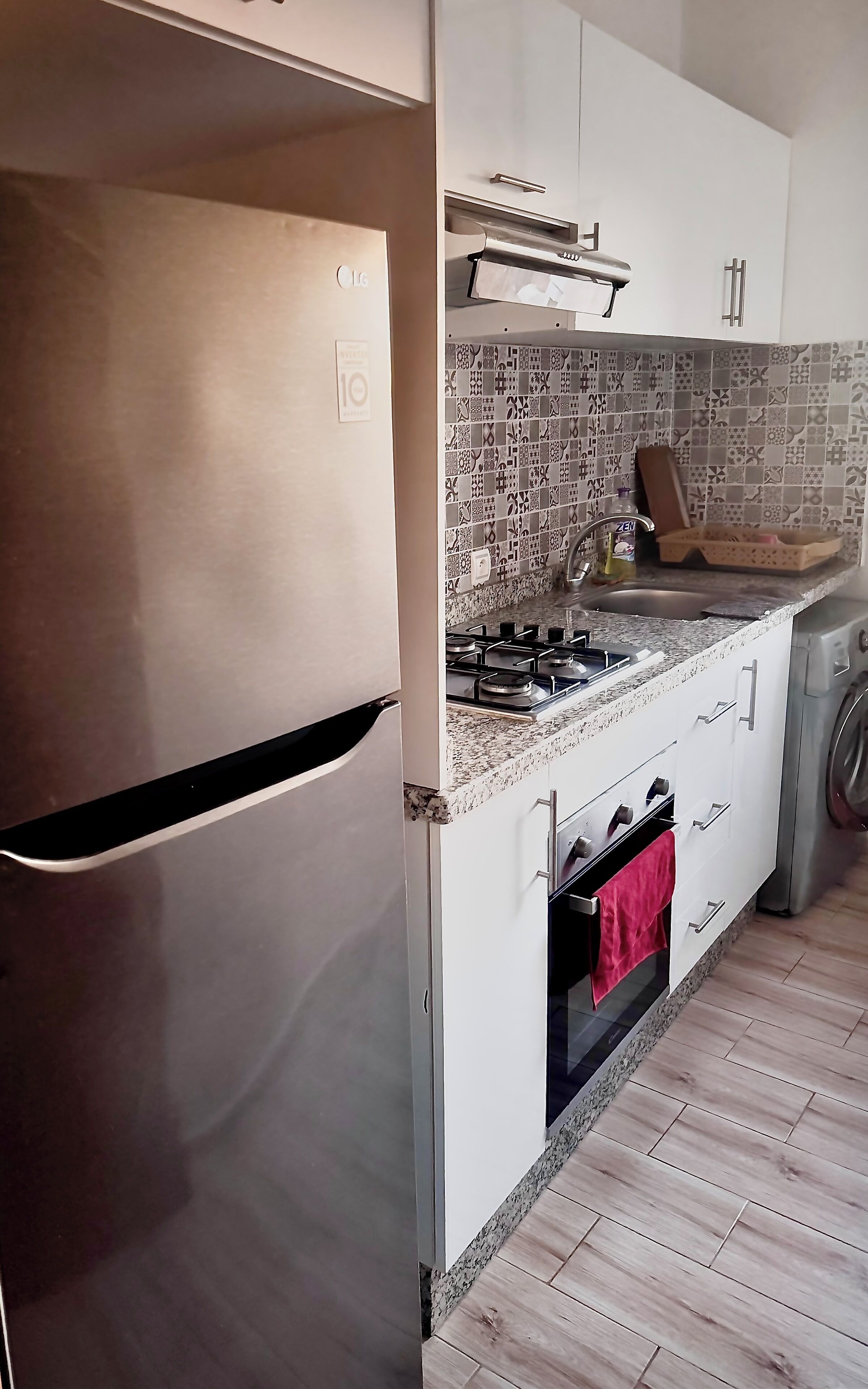 A kitchen with a stainless steel refrigerator, a gas stove, a microwave, and a washing machine.