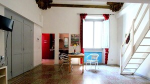 Une pièce comprenant une table à manger, deux chaises, un téléviseur et une fenêtre avec des rideaux rouges.