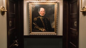 A hallway with a framed portrait on the wall, dark wooden doors, and wall sconces. - The Avery Hotel (Boise)