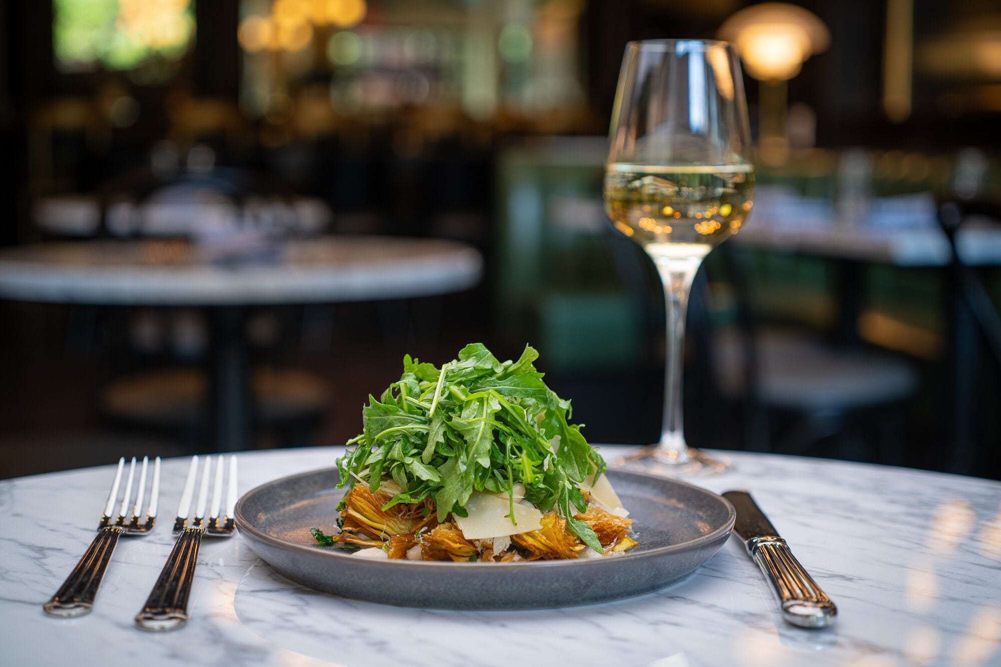 A plate of food with a glass of white wine on a marble table.