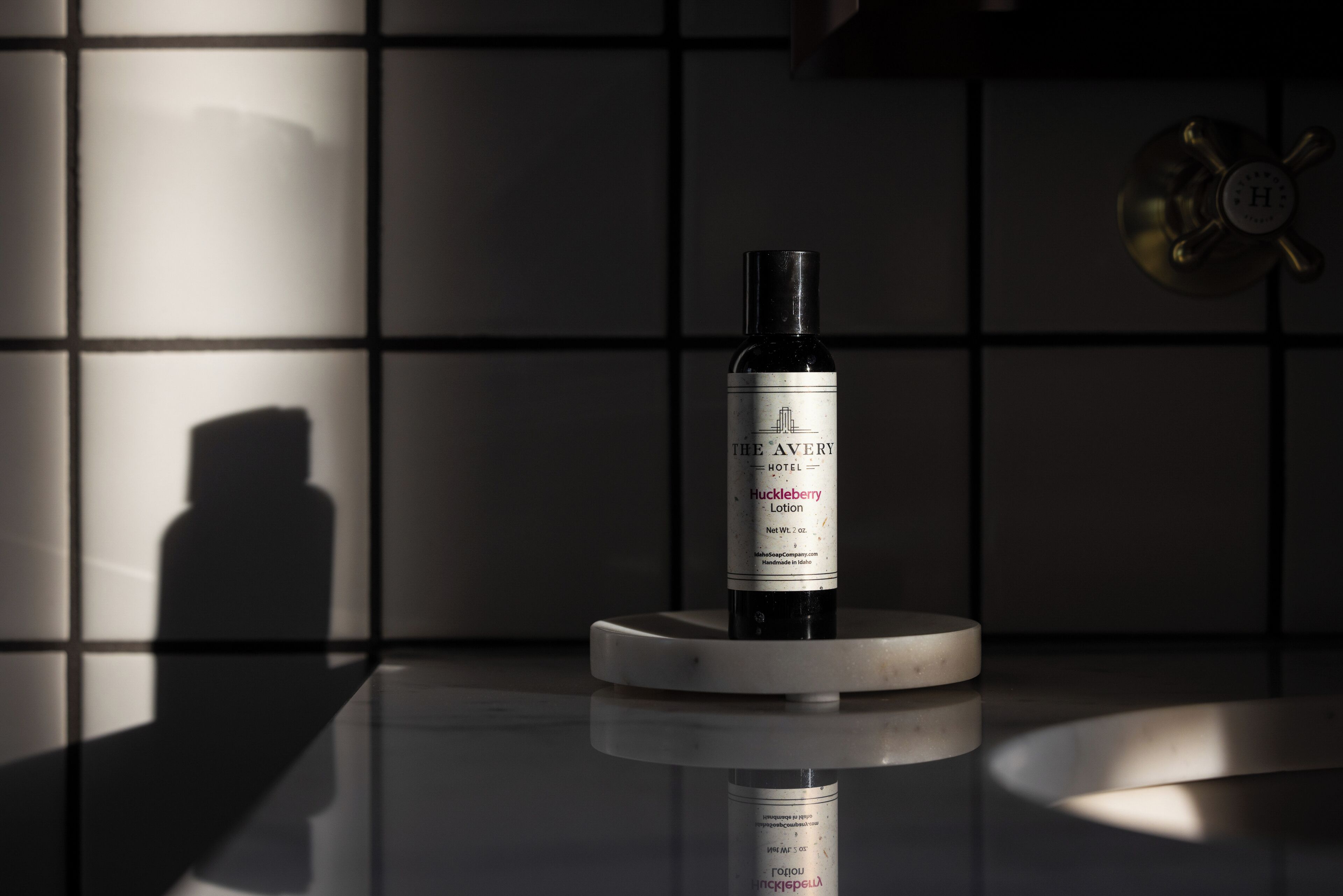 A bottle of Huckleberry Lotion on a reflective surface with a shadow of a person in the background.
