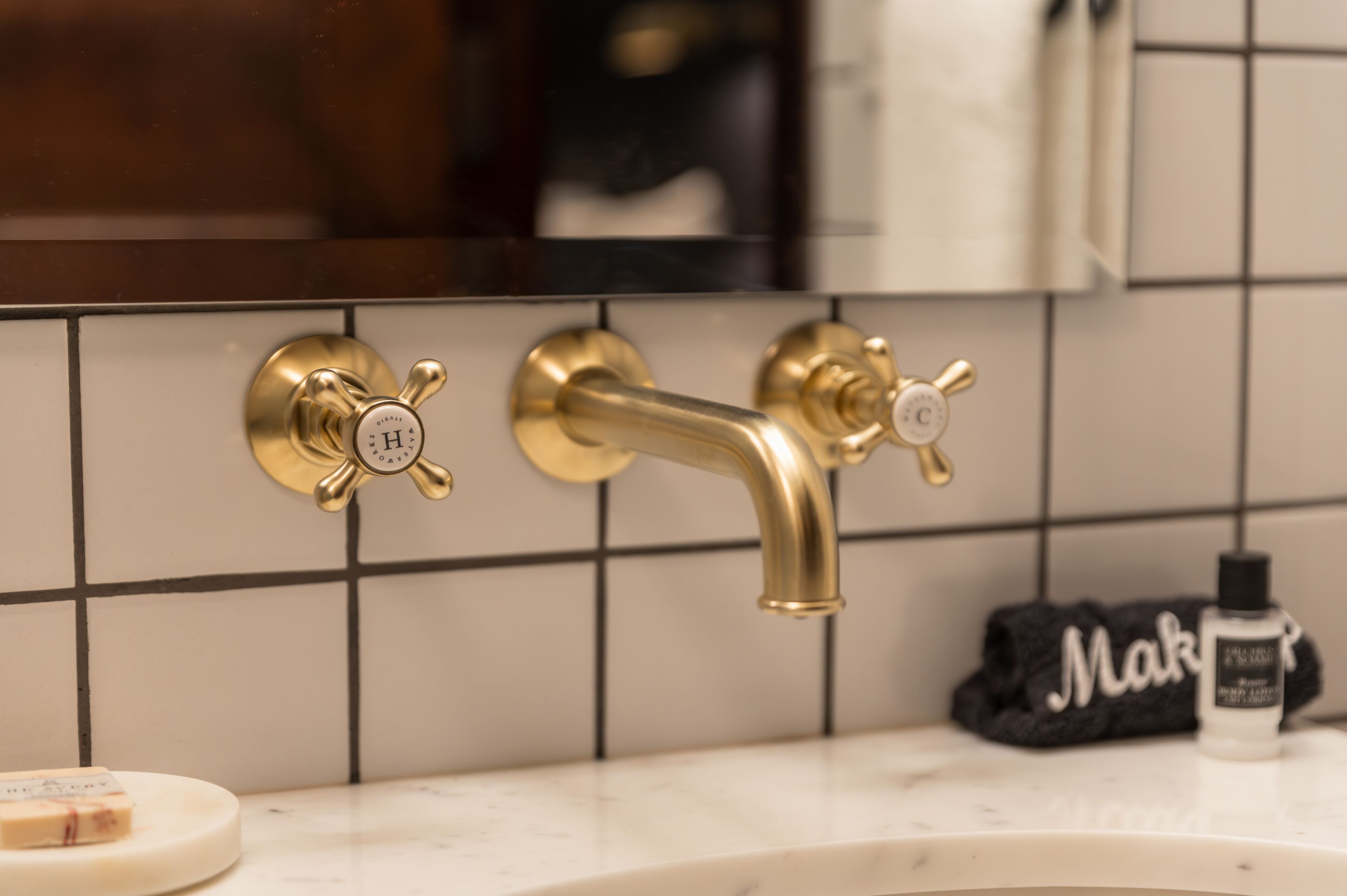 A bathroom with a gold faucet, a towel with the word "Make" on it, and a soap dish.