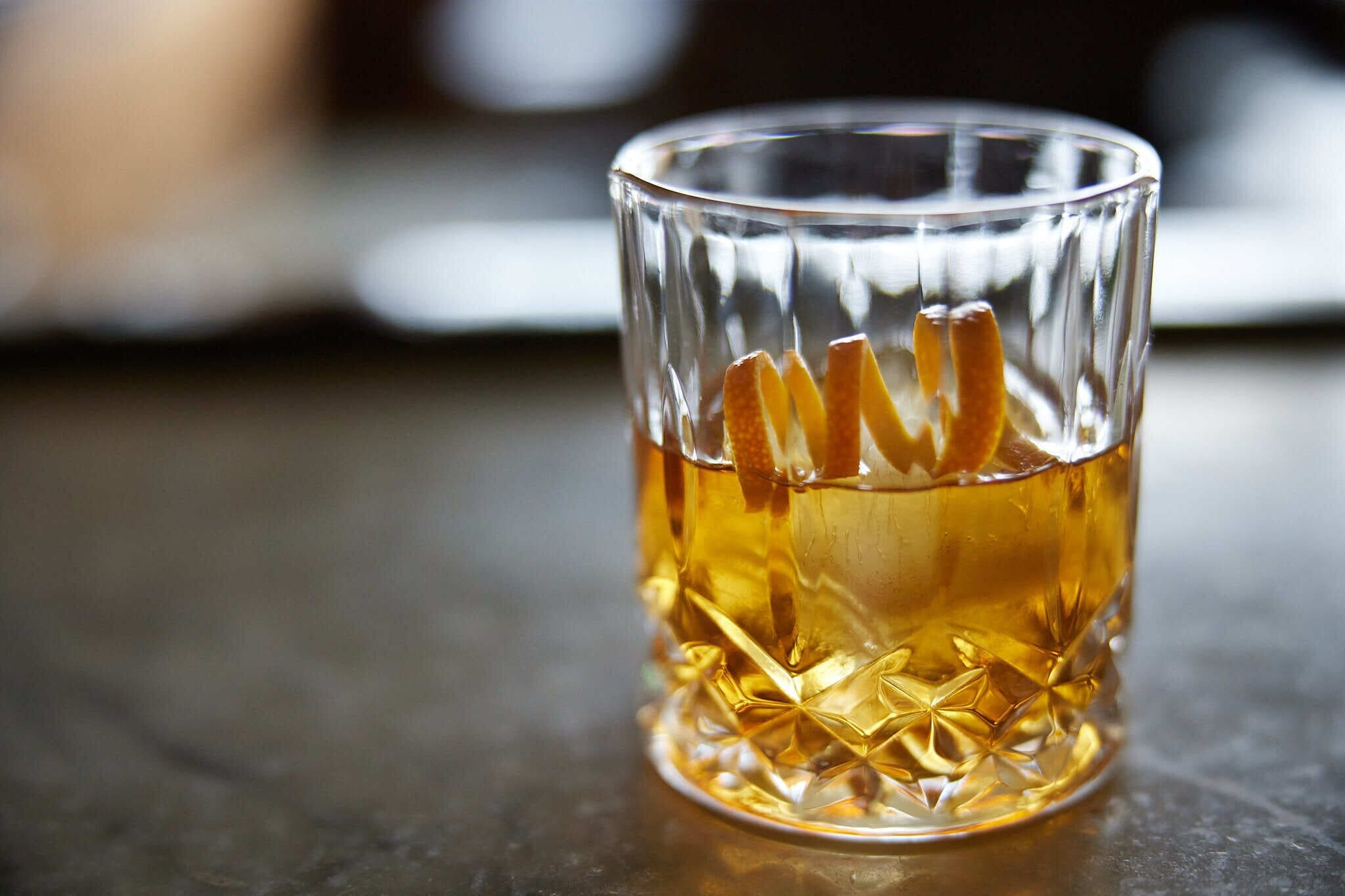 Un vaso de vidrio transparente con un diseño texturizado, lleno de un líquido dorado, sobre una superficie oscura.