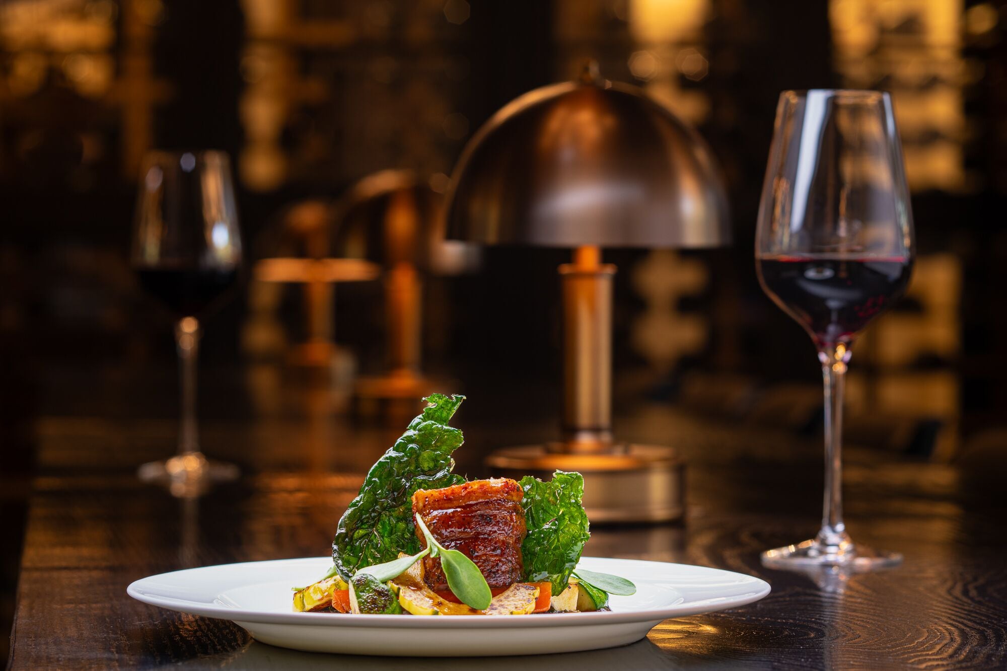 Un plato de comida con una copa de vino tinto sobre una mesa de madera.