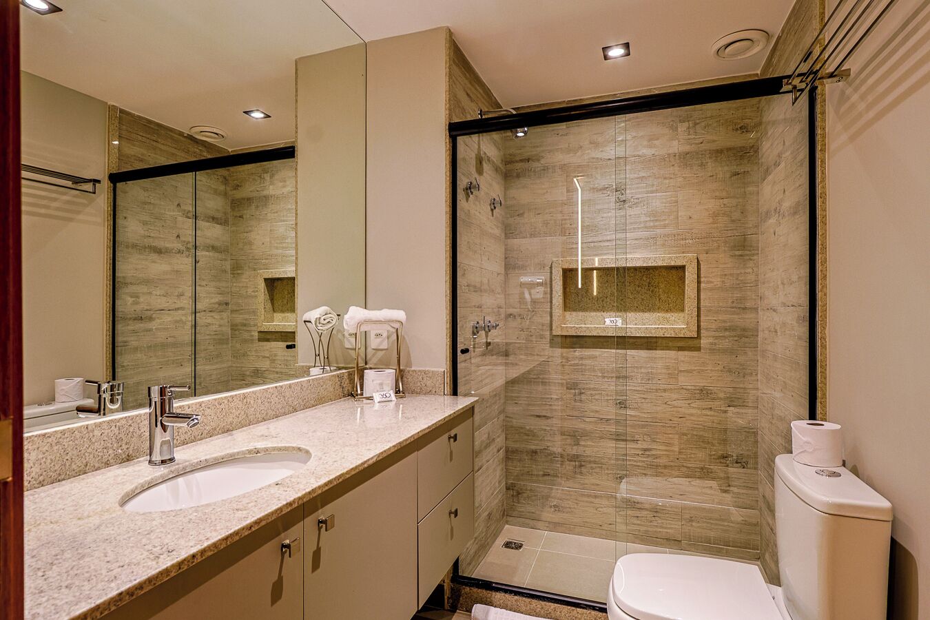 Een moderne badkamer met een wastafel met dubbele wastafel, een grote spiegel, een douche met glazen wanden en een toilet.