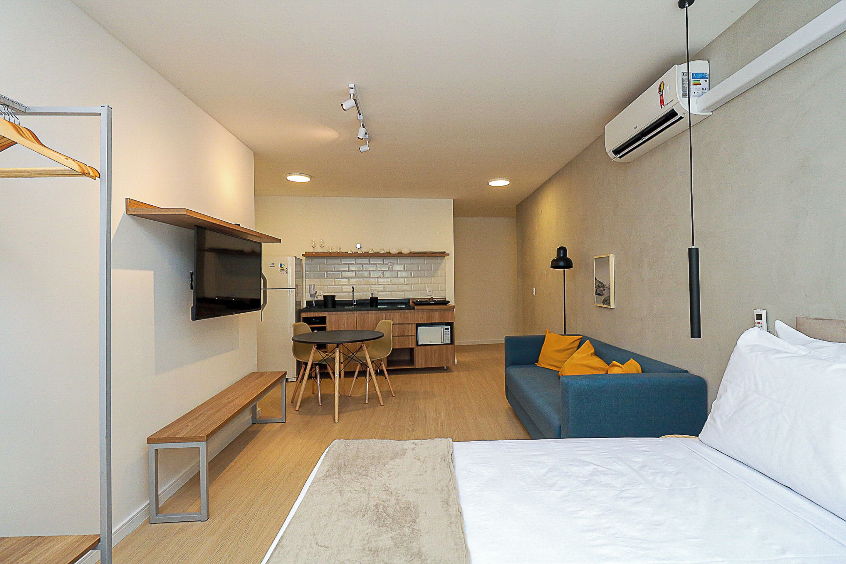 A modern hotel room with a bed, a sofa, a desk, and a kitchenette.