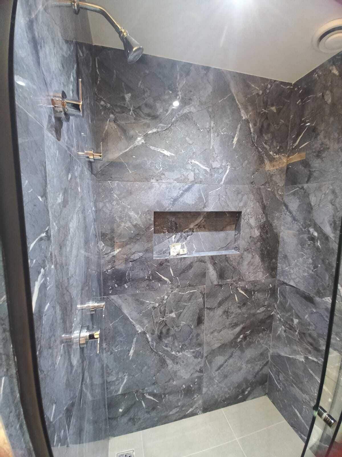 A modern shower with a glass enclosure, marble walls, and a rectangular shelf.
