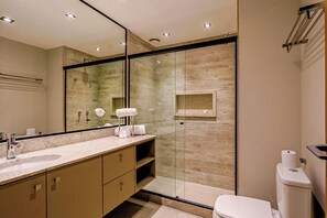 Une salle de bain moderne avec une douche à parois de verre, un grand miroir, un lavabo avec un meuble-vasque et des toilettes.
