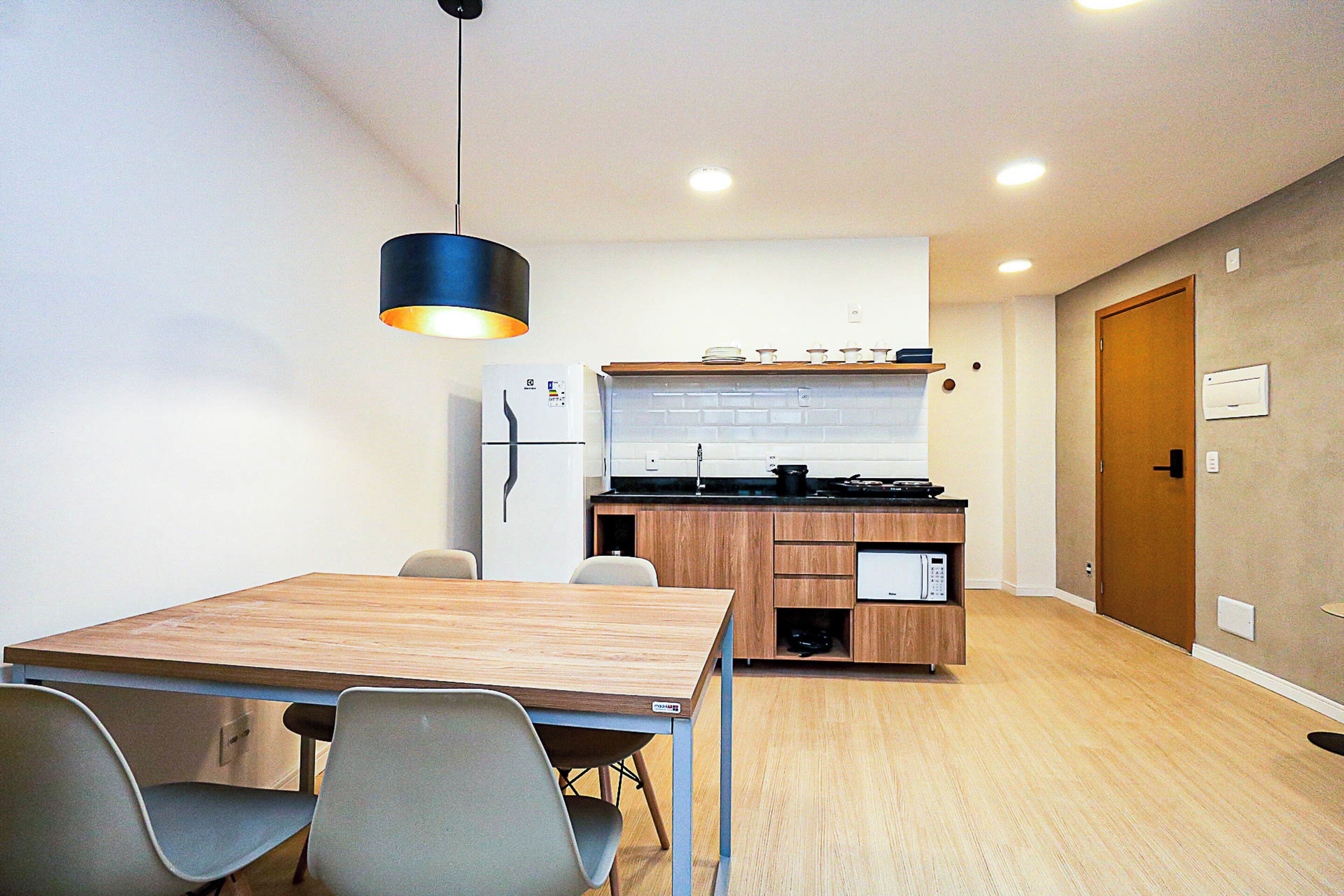 A modern kitchen with wooden cabinets, a built-in oven, and a black hanging light fixture.