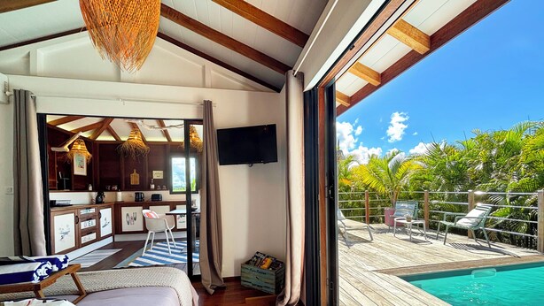 Ein Zimmer mit Bett, Schreibtisch, Fernseher und Blick auf einen Pool und tropische Pflanzen.