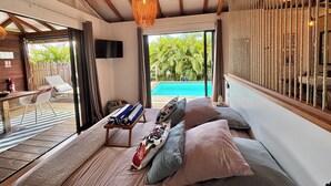 Ein modernes Schlafzimmer mit großem Bett, Blick auf einen Swimmingpool und einem Balkon mit Stuhl und Tisch.