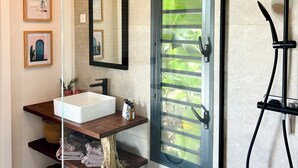 Ein modernes Badezimmer mit einem großen Spiegel, Holzregalen, einem weißen Waschbecken und einer Dusche.