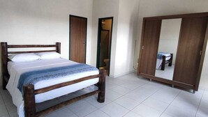 A bedroom with a wooden bed, white walls, and a large mirror on one wall. - Casa do Renato na Chapada Diamantina (Alto das Pedras Lençóis)