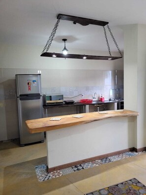 Une cuisine moderne dotée d’un îlot central en bois, d’appareils électroménagers en acier inoxydable et d’un luminaire suspendu.
