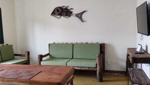 A room with a wooden table, two green patterned sofas, a wall-mounted fish sculpture, and a television on a wooden stand. - Casa do Renato na Chapada Diamantina (Alto das Pedras Lençóis)