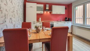 Une cuisine compacte avec des meubles blancs, un mur rouge et un coin repas comprenant une table en bois et des chaises rouges.