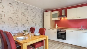 Une cuisine de taille réduite avec des meubles blancs, un mur rouge et une table à manger en bois, assortie de chaises rouges.