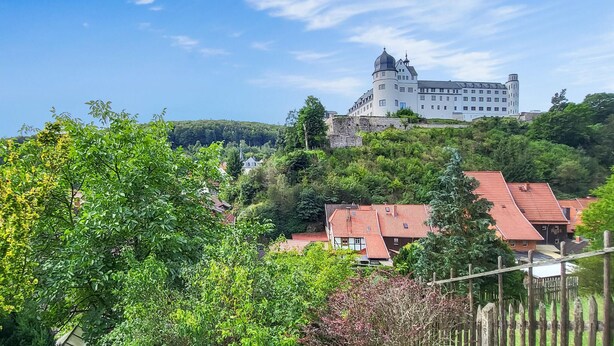 Un grand château perché sur une colline, entouré de verdure et de bâtiments traditionnels.