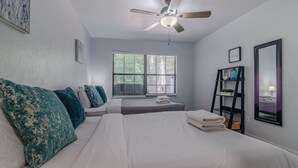 A bedroom with two beds, a ceiling fan, a window with blinds, and a black shelf with decorative items. - Gainesville Cozy Pet friendly Near UF & Downtown (Gainesville)