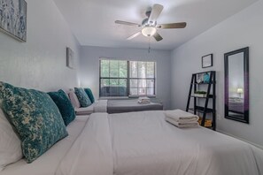 A bedroom with two beds, a ceiling fan, a window with blinds, and a black shelf with decorative items. - Gainesville Cozy Pet friendly Near UF & Downtown (Gainesville)