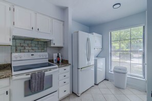 A kitchen with white cabinets, a stove, a refrigerator, and a window with blinds. - Gainesville Cozy Pet friendly Near UF & Downtown (Gainesville)