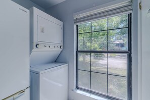 A laundry room with a front-loading washer and dryer, a window with blinds, and a view of a residential area outside. - Gainesville Cozy Pet friendly Near UF & Downtown (Gainesville)