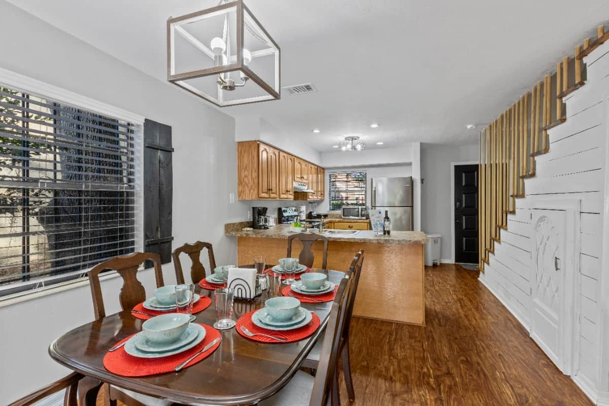 A modern kitchen with wooden cabinets, a central island, and a dining area set for six with red placemats.