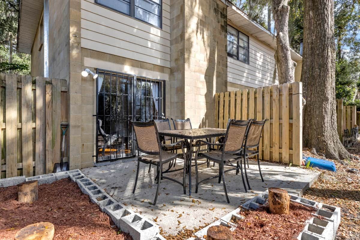 A patio with a table and chairs, a wooden fence, and a tree.