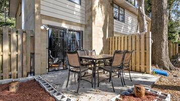 A patio with a table and chairs, a wooden fence, and a tree.