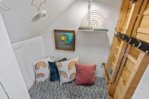 A cozy corner with a sloped ceiling, a framed picture with a star and moon, a small shelf with books, and a wooden coat rack.