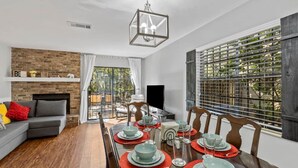A dining area with a long table set for four, a fireplace, and a view through a window with blinds. - Gainesville Nook Room (Gainesville)